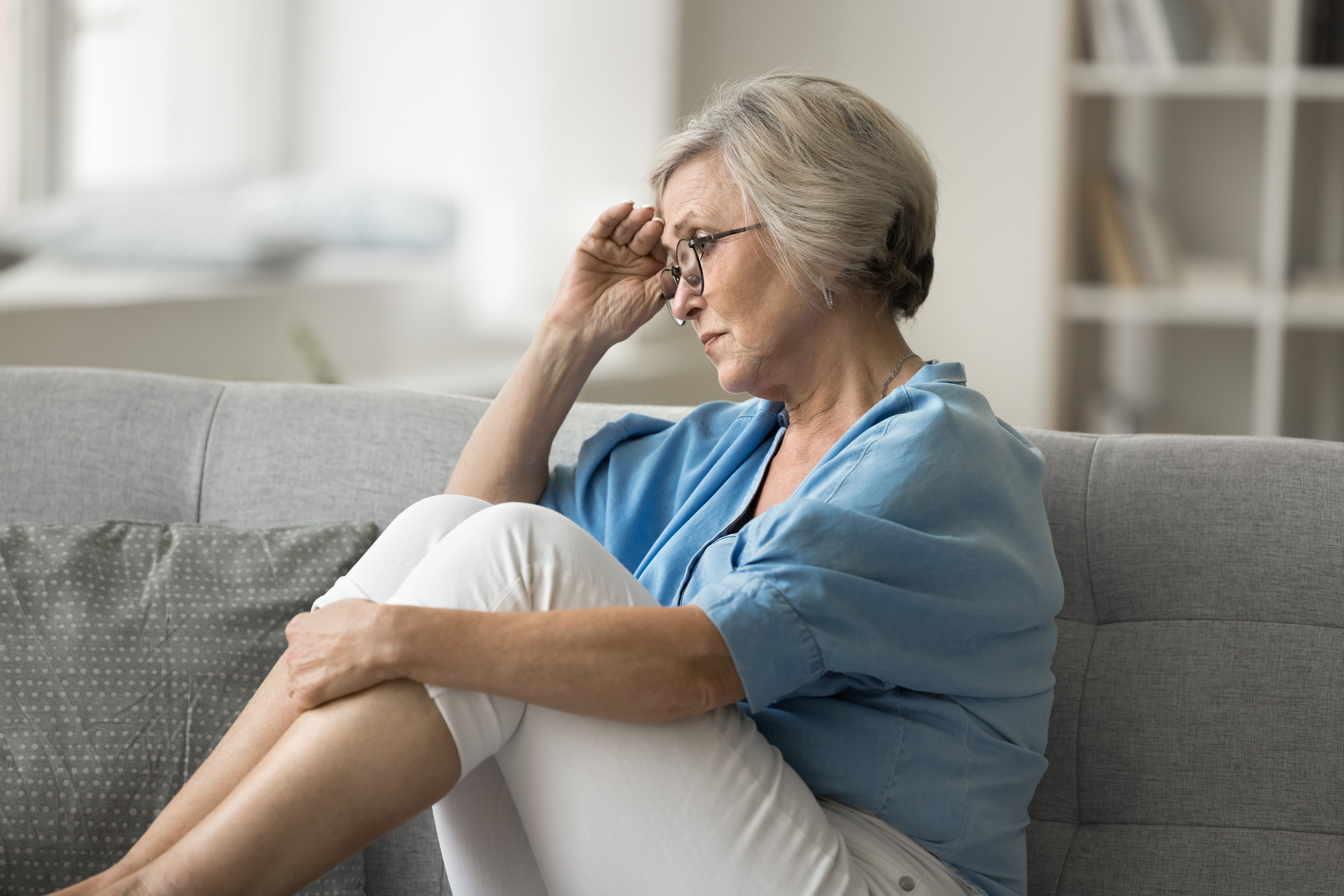 Sad aged woman sit on sofa alone in living room suffers from health issues, life difficulties or fights, retirement bring financial insecurity, causing stress and worries. Regrets, unresolved problems